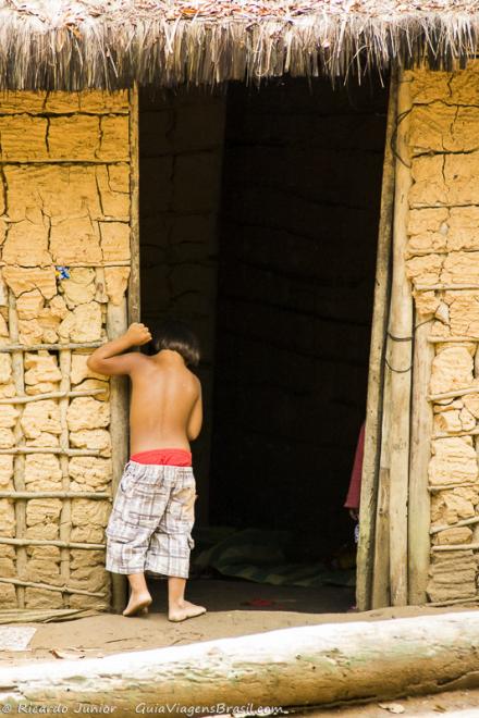 Imagem de um menino entrando na casa de barro na Aldeia Indígena.